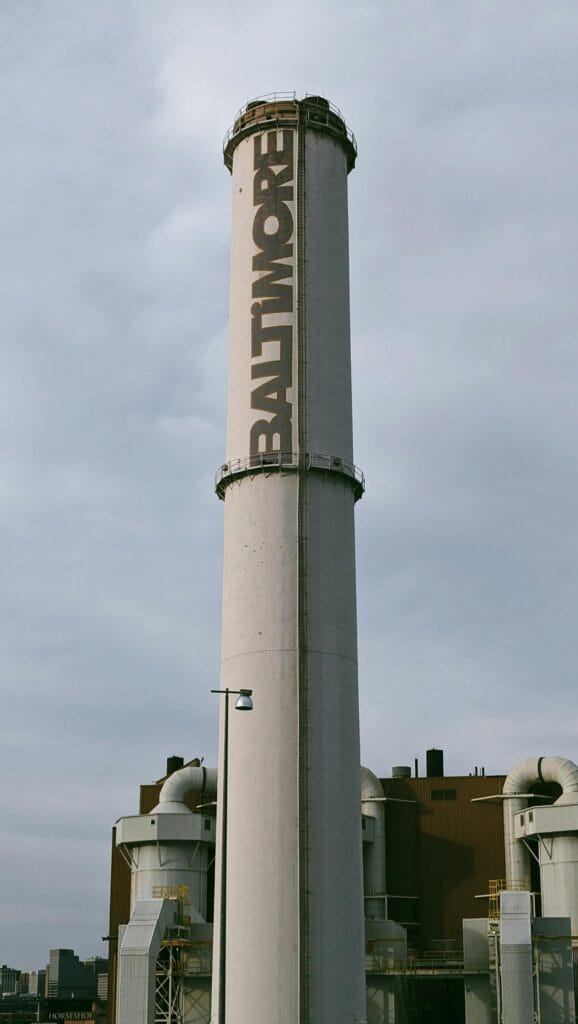 Vertical shot of Baltimore's iconic industrial tower with urban skyline under a cloudy sky.