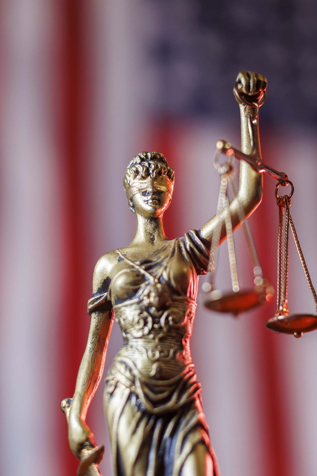 Lady Justice figure holding scales in front of a blurred American flag