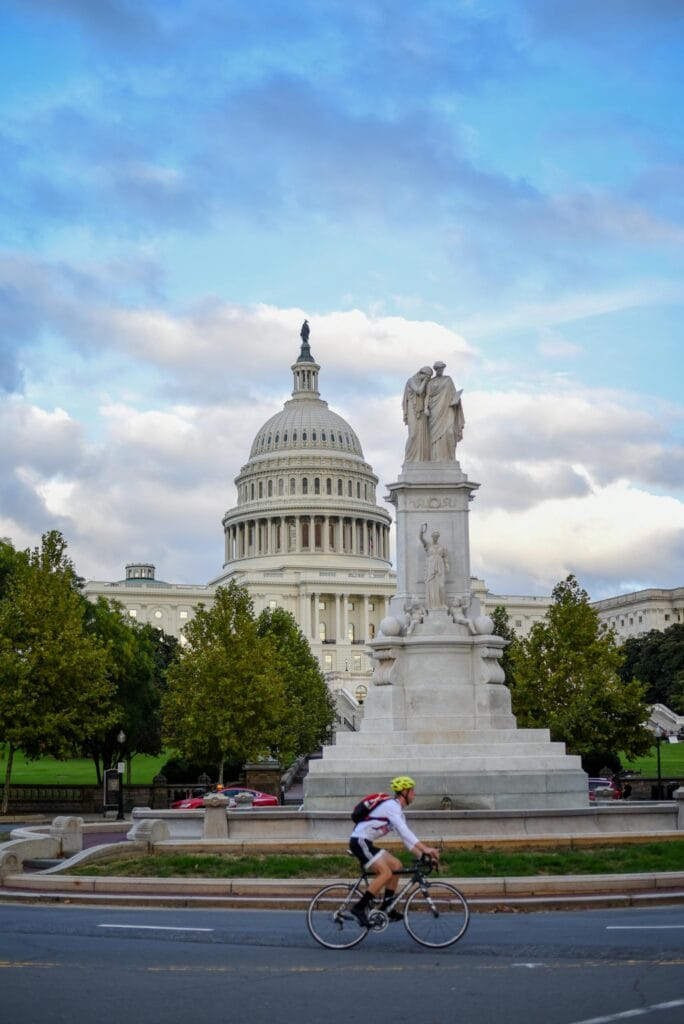 A cyclist rides past the iconic United States Capitol building on a clear day.