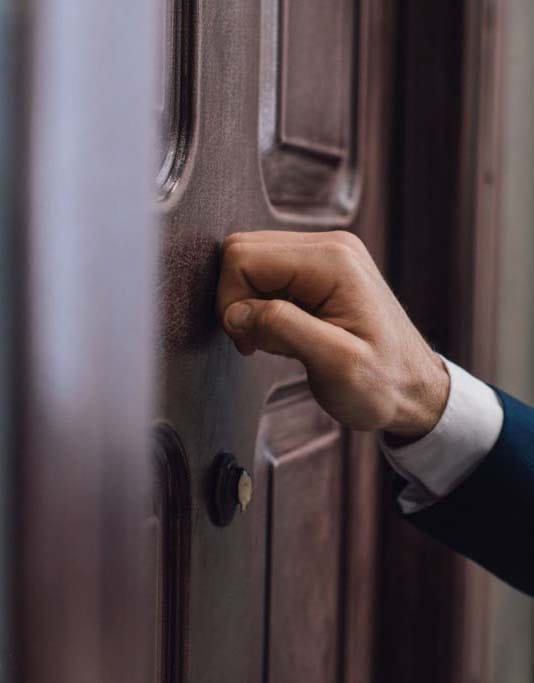 A hand knocks on a wooden door to serve a subpoena