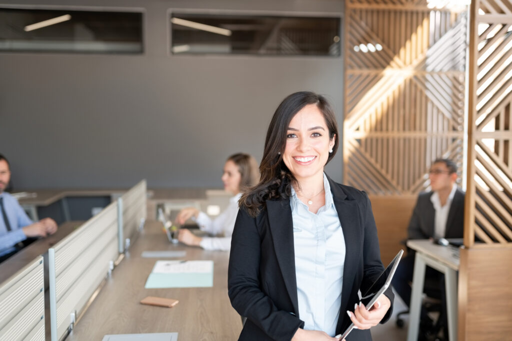 Portrait of female lawyer holding digital tablet standing in office with colleagues working in background