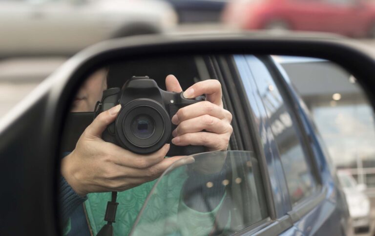 A process server photographing through car window with camera.