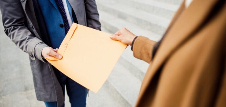 Two people exchanging a large envelope outdoors.